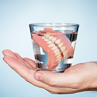 Hand holding glass with dentures in water