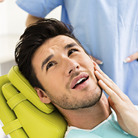 Young man in dental chair holding face