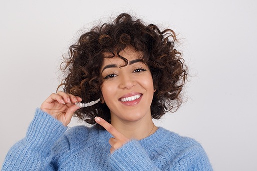 Woman wearing blue sweater and pointing to clear aligner