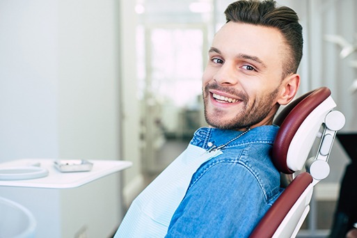 Man in denim jacket sitting in dental chair smiling