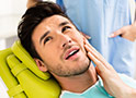 Man in dental chair holding face in pain