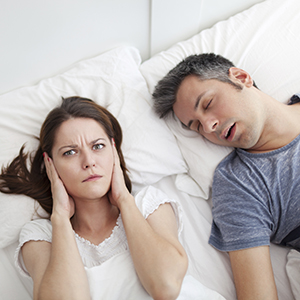 Woman covering ears in bed with snoring man