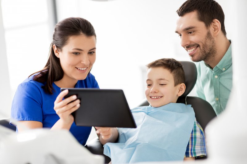 a dentist showing a boy and his father an image on a tablet