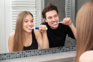 young couple brushing teeth at home in front of mirror