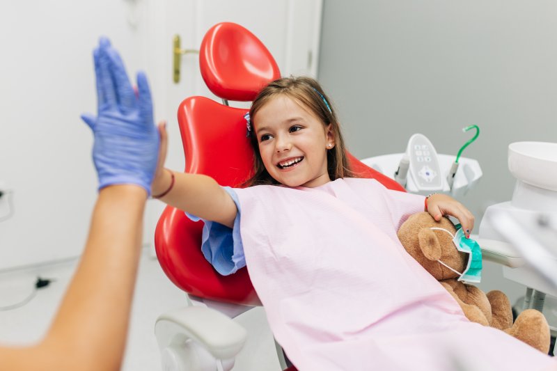 a little girl holding a teddy bear while giving her dentist a high-five