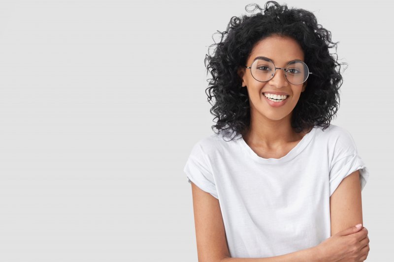 a young woman wearing a white shirt and glasses, folding her arms across her waist and smiling