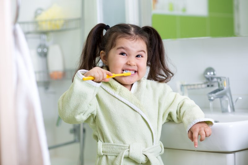 Little girl in bathrobe brushing her teeth