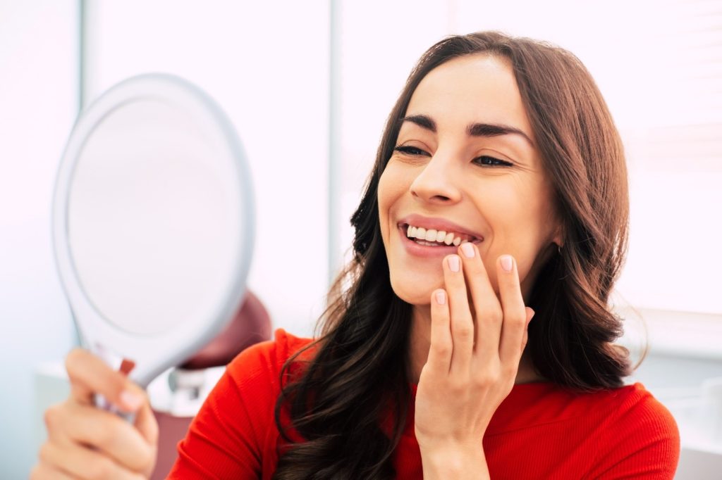 Smiling patient looking at dental implant in mirror