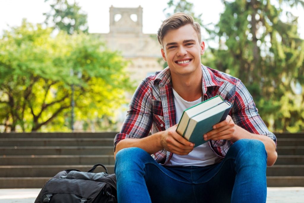 College student smiling while holding books on steps of campus